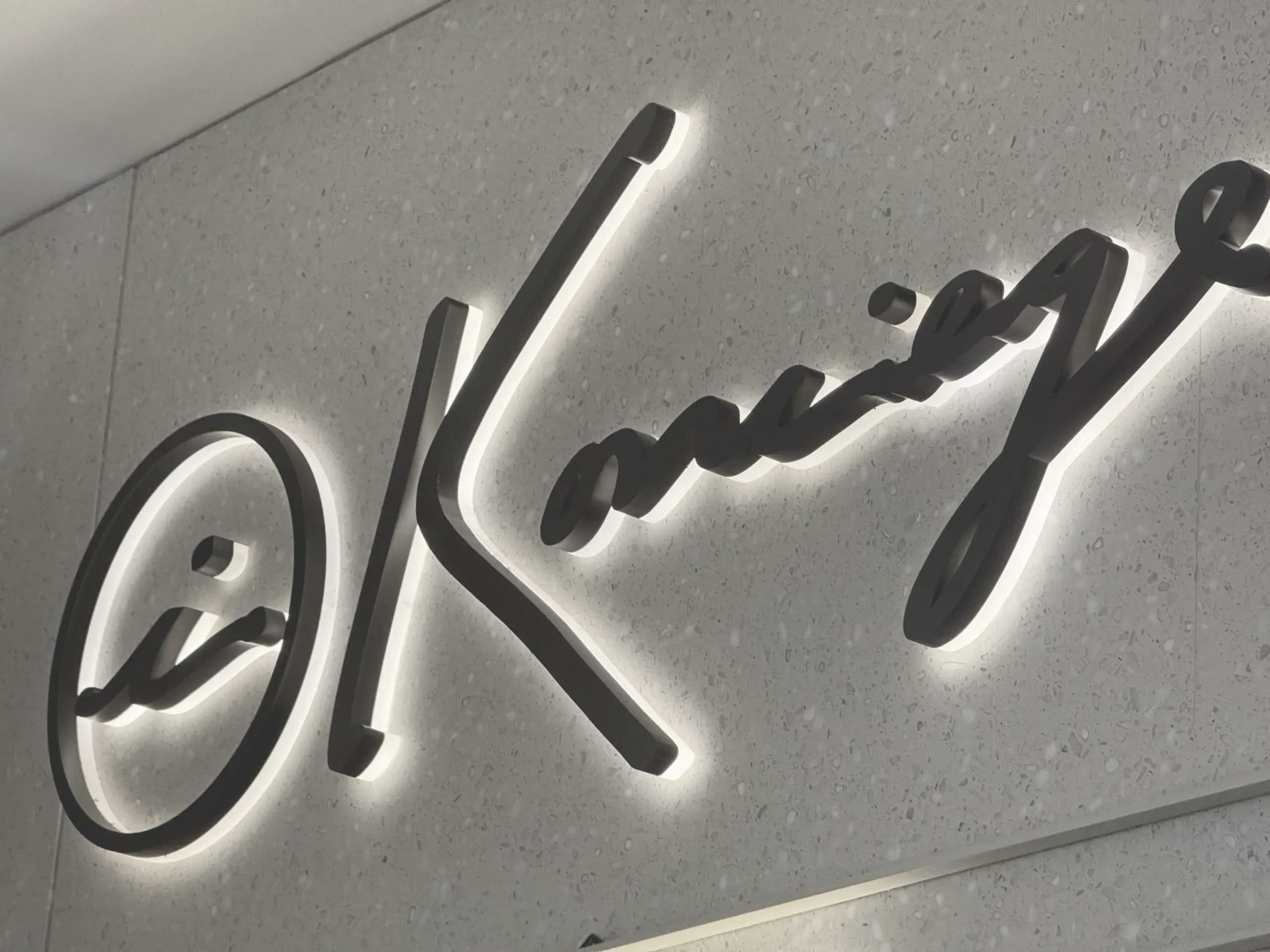 Black dimensional script letters with crisp white halo lighting on a textured wall